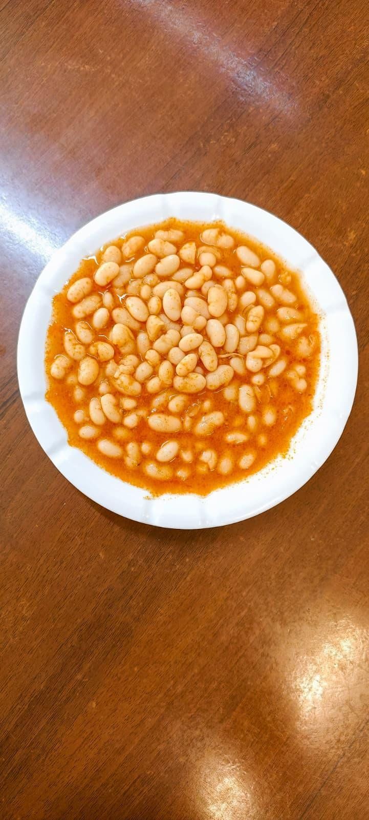 Beyaz tabakta domates soslu kuru fasulye yemeği, üzerinde kızarmış biber suyu